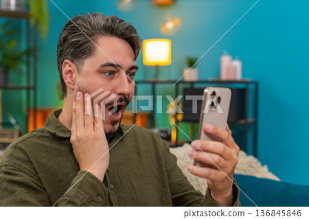 Middle-aged man shocked reading wow news on smartphone eyes wide cheering joyful surprise great win Middle-aged man shocked reading wow news on smartphone eyes wide cheering joyful surprise great win 136845846