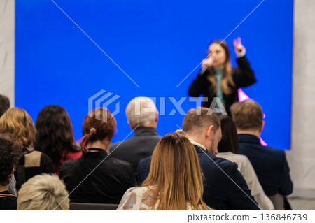 Conference speaker presents to engaged audience during a live presentation with blue backdrop 136846739