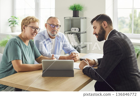 Couple signing documents with financial advisor at office desk using tablet Couple signing documents with financial advisor at office desk using tablet 136846772