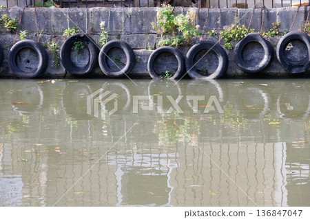 Line of old black tires protecting stone canal wall Line of old black tires protecting stone canal wall 136847047