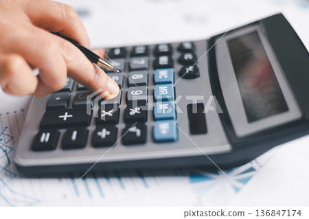 Close-up of a hand pressing calculator keys for budgeting, accounting and financial analysis. Business expense planning, tax calculation, office desk background, copy space for paperwork. Close-up of a hand pressing calculator keys for budgeting, accounting and financial analysis. Business expense planning, tax calculation, office desk background, copy space for paperwork. 136847174