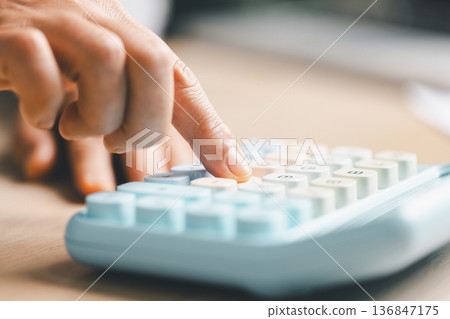 Close-up of a hand pressing calculator keys for budgeting, accounting and financial analysis. Business expense planning, tax calculation, office desk background, copy space for paperwork. Close-up of a hand pressing calculator keys for budgeting, accounting and financial analysis. Business expense planning, tax calculation, office desk background, copy space for paperwork. 136847175