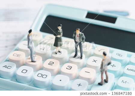 Miniature business people standing on calculator keys with financial report background, symbolizing accounting, budgeting and audit teamwork. Tax calculation, analytics and office finance copy space. 136847180