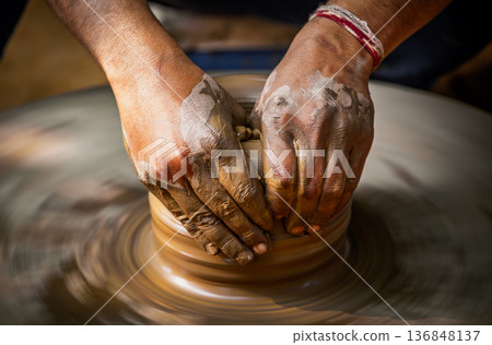 Skilled artisan hands shaping wet clay on a spinning potter wheel, creating a ceramic vase in a traditional pottery workshop. Skilled artisan hands shaping wet clay on a spinning potter wheel, creating a ceramic vase in a traditional pottery workshop. 136848137