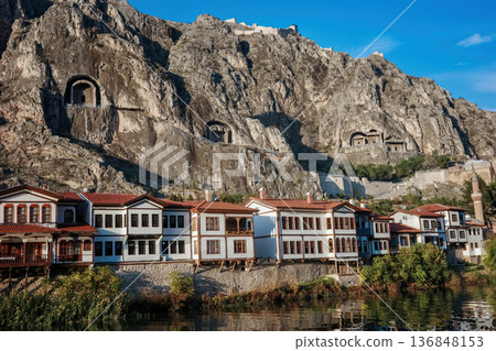 Ancient rock-cut tombs carved in cliff face above Amasya city with traditional Ottoman houses, mosque with minaret below in valley, heritage and historical architecture concept Ancient rock-cut tombs carved in cliff face above Amasya city with traditional Ottoman houses, mosque with minaret below in valley, heritage and historical architecture concept 136848153