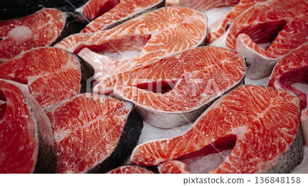 Fresh raw salmon steaks on display, bright orange fish meat with marble texture and skin, ready for cooking, seafood market background. Fresh raw salmon steaks on display, bright orange fish meat with marble texture and skin, ready for cooking, seafood market background. 136848158