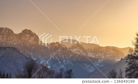 Giewont peak in Tatra Mountains above Zakopane town in Poland, Europe. An ethereal landscape with the snowy mountains rising beneath a sun-kissed sky at early morning or late afternoon. 136849199