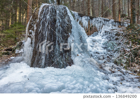 Icy cascade nestled amidst a serene forest, showcasing the stark beauty of winter's embrace. Icicles cling, transforming the landscape into a wonderland of water and ice. Icy cascade nestled amidst a serene forest, showcasing the stark beauty of winter's embrace. Icicles cling, transforming the landscape into a wonderland of water and ice. 136849200