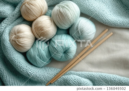 Skeins of yarn and knitting needles resting on knitted fabric 136849302