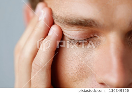 Male patient closing one eye during a vision test, holding his head with one hand, with a neutral background emphasizing the examination context 136849566
