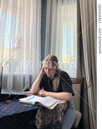 Focused woman writing notes in notebook while sitting at table at home. 136850485