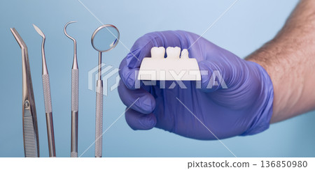 Dentist Hand in Blue Medical Glove Holding Dental Crown Shade or Prosthetic Tooth Model with Dental Instruments on Light Blue Background Dentist Hand in Blue Medical Glove Holding Dental Crown Shade or Prosthetic Tooth Model with Dental Instruments on Light Blue Background 136850980