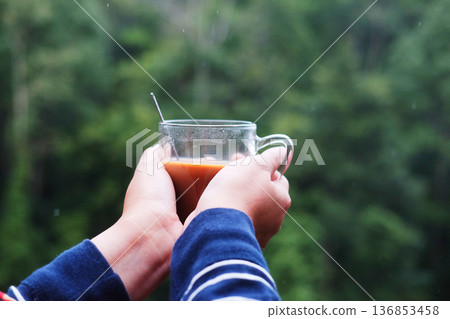 Hand holding a glass cup of hot coffee in tropical green forest background 136853458