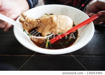 Hand holding Chicken thighs of Noodles with braised chicken in white bowl 136853465