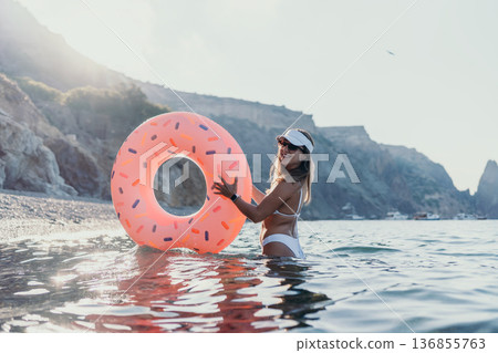 Woman, donut float, beach. Happy woman holding inflatable donut in sea near rocky cliffs, enjoying summer vacation. Woman, donut float, beach. Happy woman holding inflatable donut in sea near rocky cliffs, enjoying summer vacation. 136855763