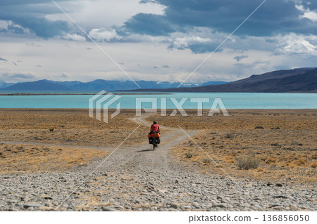 Cyclist riding remote gravel track toward turquoise Lago Argentino, Patagonia Cyclist riding remote gravel track toward turquoise Lago Argentino, Patagonia 136856050