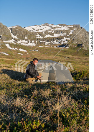 Male hiker cooking at wild camp in mountains above Hardangerfjord, Norway Male hiker cooking at wild camp in mountains above Hardangerfjord, Norway 136856093