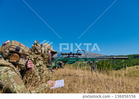 Military Snipers in Camouflage Positioned in Field Observing Targets With Precision Rifle and Spotter Military Snipers in Camouflage Positioned in Field Observing Targets With Precision Rifle and Spotter 136856556