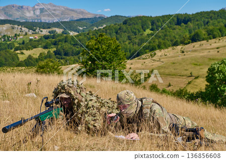 Military Snipers in Camouflage Ghillie Suits Lying in a Grass Field on a Mountain Hillside Military Snipers in Camouflage Ghillie Suits Lying in a Grass Field on a Mountain Hillside 136856608
