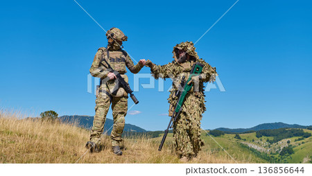 Two Soldiers in Camouflage and Ghillie Suit Fist Bumping During Mountain Training Exercise With Sniper Rifle 136856644