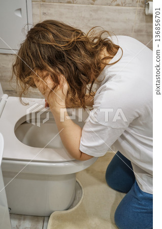 Woman experiencing nausea and vomiting into toilet bowl Woman experiencing nausea and vomiting into toilet bowl 136856701