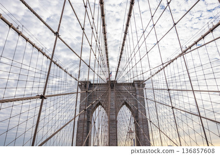 Brooklyn Bridge pedestrian walkway perspective with suspension cables and stone towers against cloudy sky in New York City USA Brooklyn Bridge pedestrian walkway perspective with suspension cables and stone towers against cloudy sky in New York City USA 136857608
