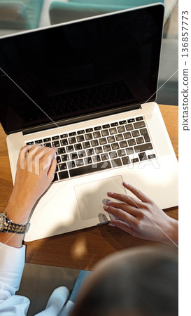 User works on laptop at a desk during daytime 136857773