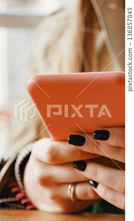 Person holds a pink smartphone with black nails in a casual setting during the day Person holds a pink smartphone with black nails in a casual setting during the day 136857845