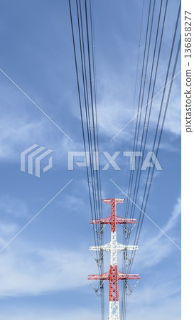 A top-down view of red and white power transmission towers and power lines against a blue sky 136858277