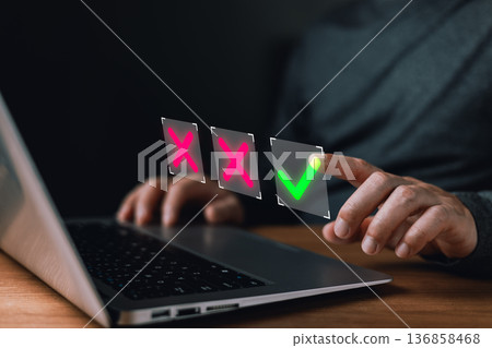 person interacts with a laptop selecting a glowing green checkmark among red X symbols representing decision making,approval processes,rejection choices,verification,and digital confirmation workflow. 136858468