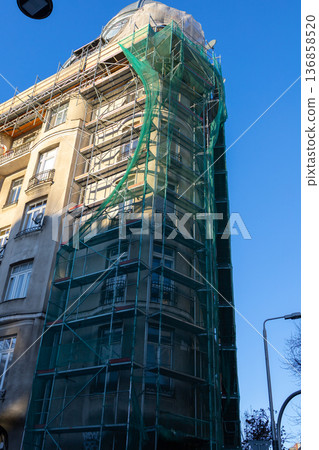 Building renovation with scaffolding and green mesh in urban area Building renovation with scaffolding and green mesh in urban area 136858520