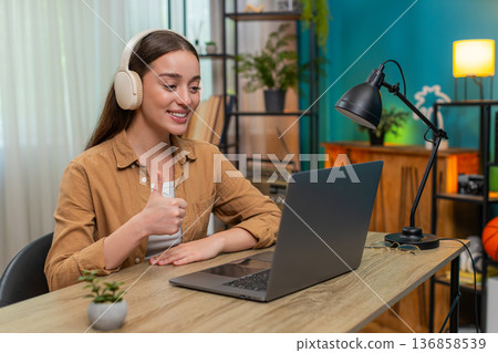 Young woman on laptop video call wearing wireless headset speaking live providing customer support Young woman on laptop video call wearing wireless headset speaking live providing customer support 136858539