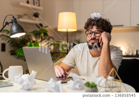 Arabian man fights creative block writes ideas for project crumpled papers desk frustrated evening Arabian man fights creative block writes ideas for project crumpled papers desk frustrated evening 136858545