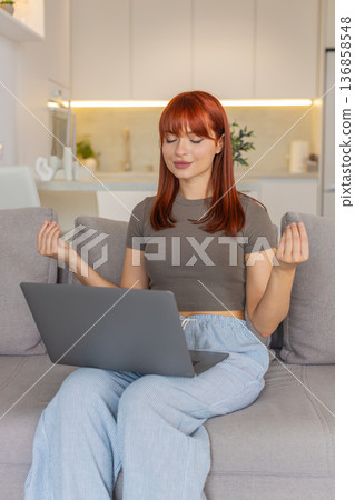 Young woman takes break from laptop work does meditation deep breathing and tries to calm down focus 136858548
