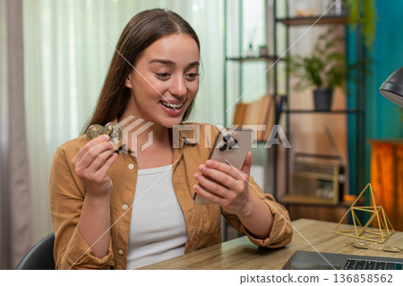 Young woman celebrates bitcoin sale smiling at smartphone graph showing crypto profit growth today Young woman celebrates bitcoin sale smiling at smartphone graph showing crypto profit growth today 136858562