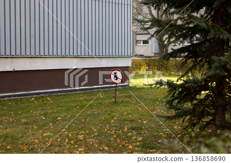 No dogs allowed sign stands in a grassy area near a building 136858690