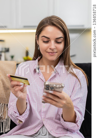 Young woman pays online order with smartphone and credit card taps pay smiles after secure purchase 136858718