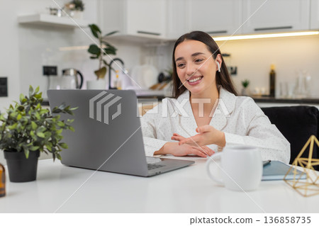 Young woman greets laptop webcam waves hand smiles starts online meet with colleagues friendly talk 136858735