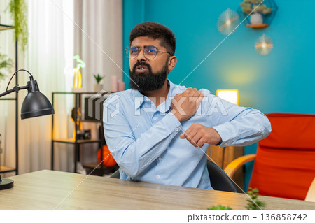 Indian man clutching painful shoulder injury sharp discomfort strained muscle seeking relief indoors Indian man clutching painful shoulder injury sharp discomfort strained muscle seeking relief indoors 136858742