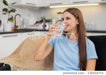 Young woman drinks water from glass keeps hydration good habit healthy lifestyle uses filter system Young woman drinks water from glass keeps hydration good habit healthy lifestyle uses filter system 136858753