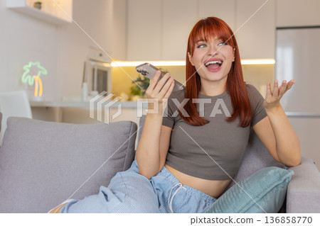 Young woman on smartphone speakerphone joyful call shares good news gestures with hands open smile 136858770