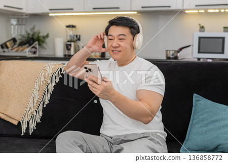 Asian man with wireless headphones enjoys playlist relaxes closes eyes rocks gently and smiles calm Asian man with wireless headphones enjoys playlist relaxes closes eyes rocks gently and smiles calm 136858772
