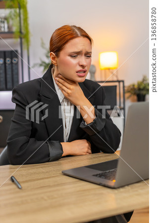 Young businesswoman touches sore throat while working on laptop then sips warm ginger tea for relief Young businesswoman touches sore throat while working on laptop then sips warm ginger tea for relief 136858780