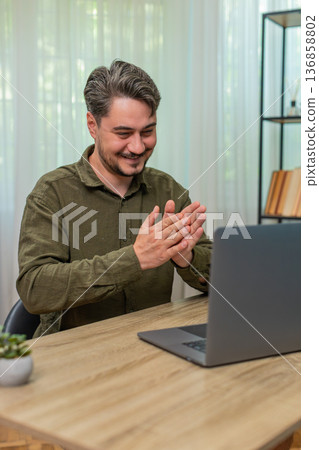 Middle-aged man pleased clasping hands reviewing laptop report celebrates big deal closure at table Middle-aged man pleased clasping hands reviewing laptop report celebrates big deal closure at table 136858802