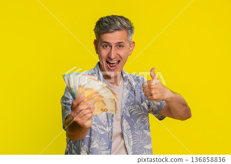 Adult man jumping with joy waving and holding euro cash celebrating win in lottery game or jackpot 136858836