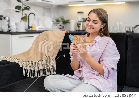 Young woman counts cash euros smiles about salary savings bonus plans dream purchase and investments 136858847