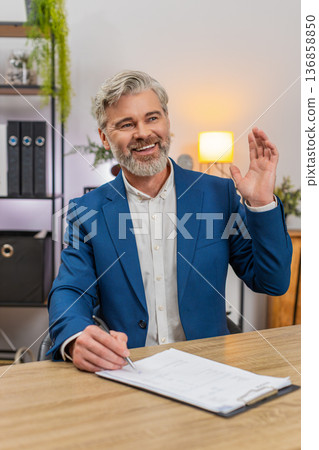 Middle-aged businessman signs document then dances laughing celebrating project completion triumph Middle-aged businessman signs document then dances laughing celebrating project completion triumph 136858850
