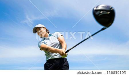 一位女子揮桿擊球，迎著藍天。一號木桿擊球。運動。清新。生活方式。素材。 136859105
