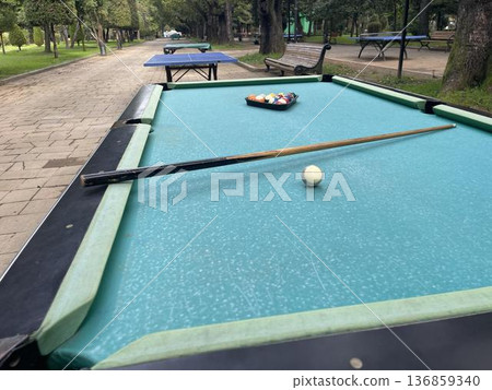 A pool table with balls and a cue in a city amusement park 136859340
