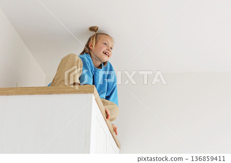 Child young girl climbing on a high cabinet having fun Child young girl climbing on a high cabinet having fun 136859411
